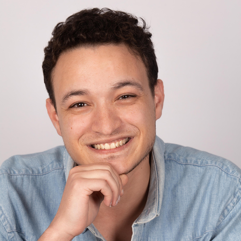 photo de face d'un jeune homme en chemise bleue, une main sous le menton